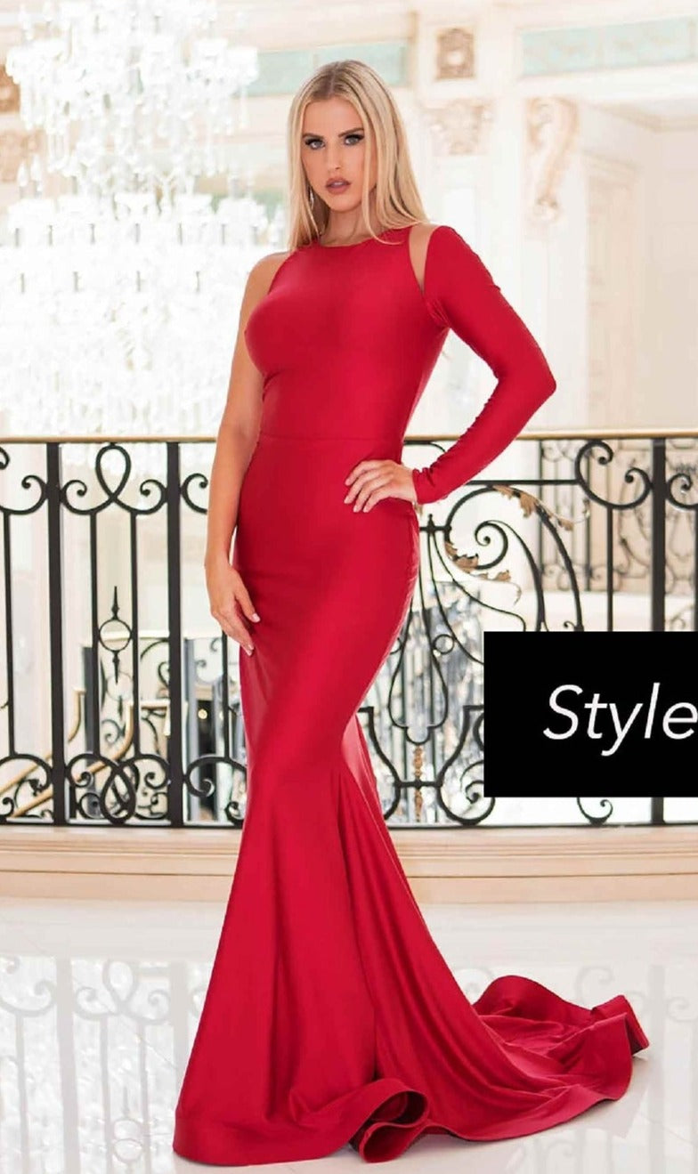Woman wearing the Jessica Angel 563: a fitted, floor-length red prom dress with one sleeve and shoulder cutouts, posing indoors by an ornate railing and chandelier.